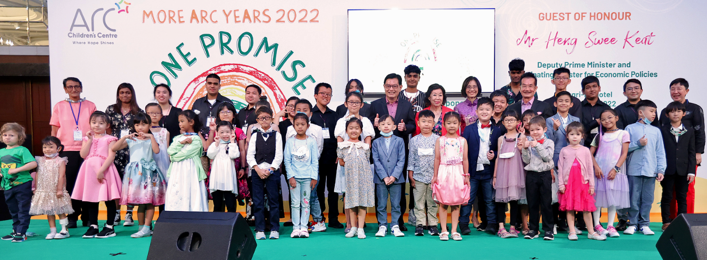 Group of children and adults posing on a stage for "ARC Children's Centre" event.